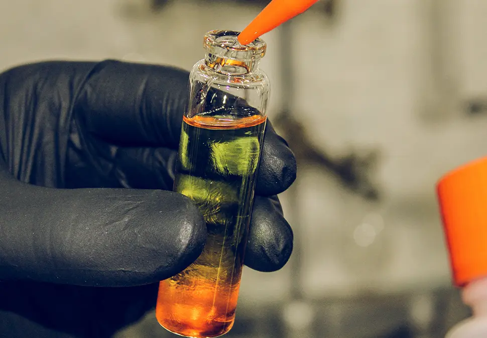 Hand with gloves holding a glass tube with cologne ingredients being put into it