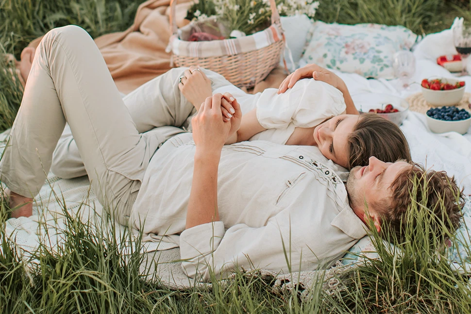 Man and woman laying down having a picnic, they are holding hands