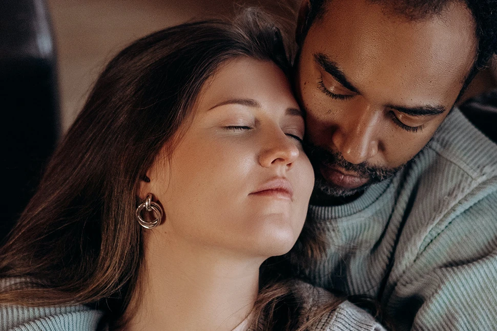 Man is holding a woman from behind, she is leaning back into him with her eyes closed