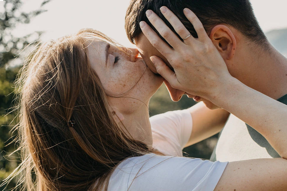 Woman holding a mans head and kissing it as he smiles