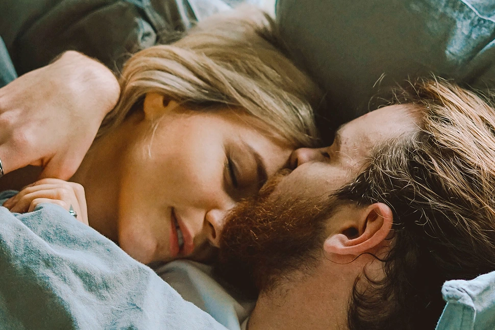 Man and woman in bed, the man is kissing the womans head, her eyes are closed