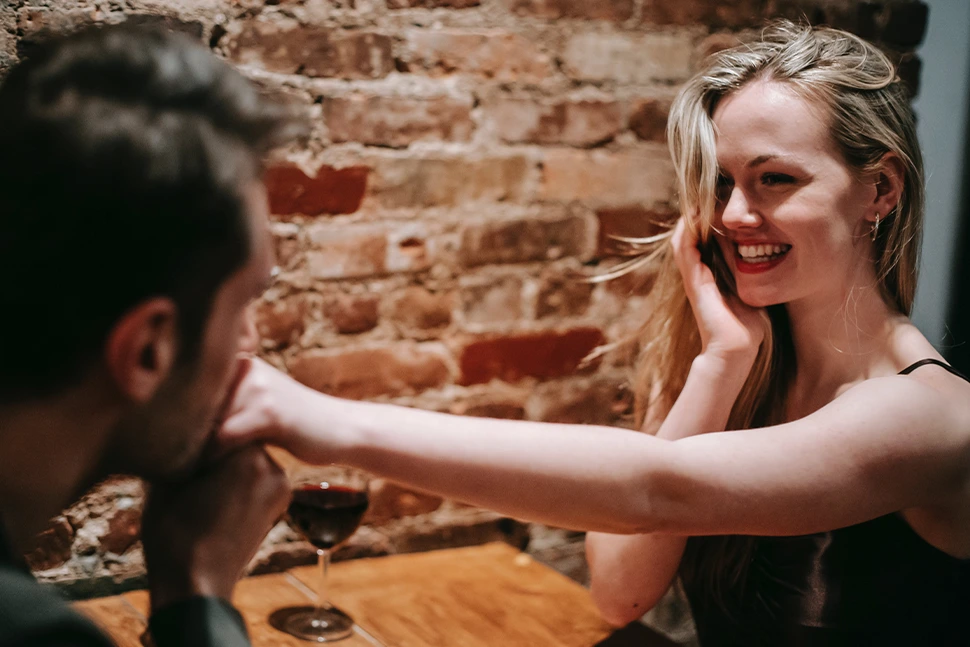 A man holding and kissing a womans hand while she smiles at him